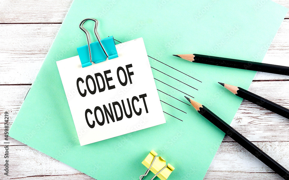 Aufkleber stickers with pencils and notebook with text code of conduct on wooden background