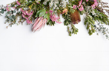 Beautiful fresh floral flat-lay arrangement of Australian native Eucalyptus leaves, pink Protea, purple Banksia, white Tea Tree and pink Wax-flowers, on a rustic white background. 