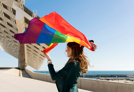 Woman holding rainbow flag near solar energy panel during sunny day