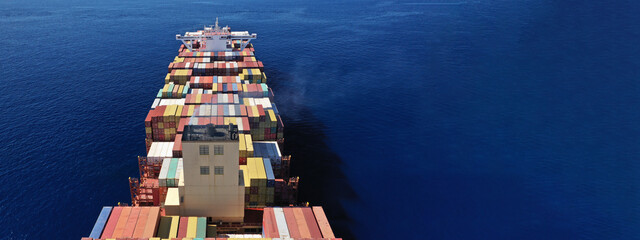 Aerial drone ultra wide panoramic view above huge colourful container carrier vessel cruising deep...