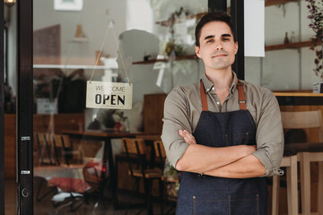 Obraz premium Portrait of a handsome and confident cafe owner standing at the door. Young man standing with his arms crossed looking at camera smiling.
