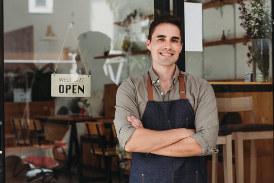 Portrait of a handsome and confident cafe owner standing at the door. Young man standing with his arms crossed looking at camera smiling.