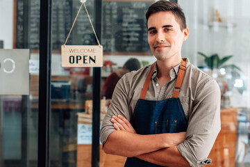 Portrait of a handsome and confident cafe owner standing at the door. Young man standing with his...