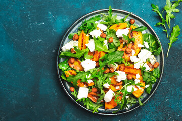 Grilled peach salad with feta cheese, hazelnuts and arugula on blue background, top view, copy space