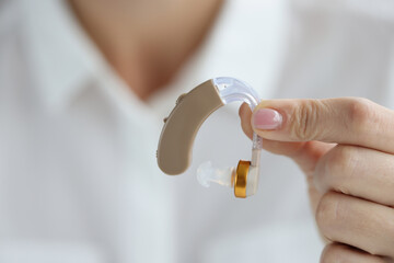 Woman holds hearing aid in hand closeup
