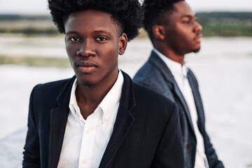 Two trendy African black men, outdoors, in stylish classic clothes, with fashionable hairstyle