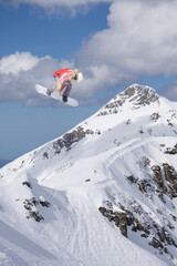 Fototapeta na wymiar A jumping snowboarder in the mountains. Snowboarding, winter extreme sport.