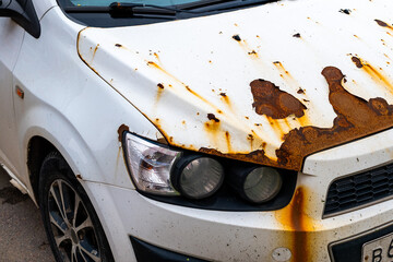 An old abandoned rusty white car with damaged paintwork on the bumper and hood.