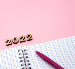 Notepad and Pen on Pink. Wooden numbers 2022. Notepad on a spring. Pink Pen. Spiral spiral checkered sheets.