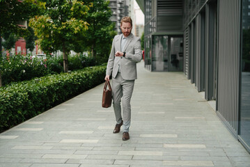 Young businessman with briefcase. Handsome man in suit watching at wristwatch