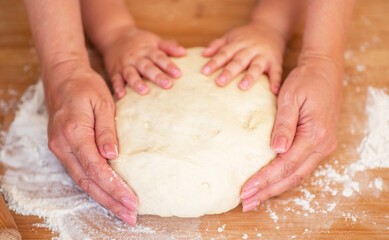 Mother and child hands prepares the dough with flour on rustic wooden table from above. Homemade pastry for bread or pizza. Bakery background.