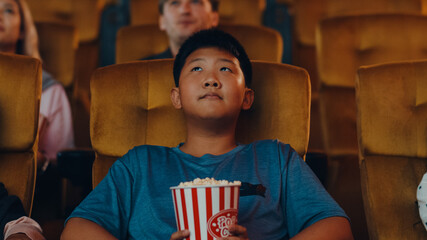 Handsome cheerful young asian boy laughing while watching film in movie theater. Lifestyle...