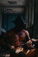 Fototapeta na wymiar Bloody zombie monster in mask sits with saw in dark room.