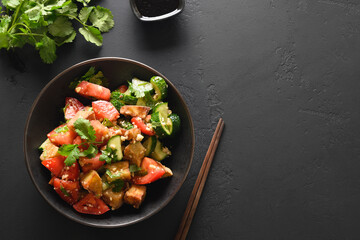 Chinese crispy spicy fry eggplant with cucumber, garlic, tomatoes, fresh cilantro leaves in oyster sauce and black vinegar on black background. View from above. Copy space.