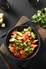 Chinese crispy spicy fry eggplants with cucumbers, garlic, tomatoes, fresh cilantro leaves in oyster sauce and black vinegar on black background. View from above. Vertical format.