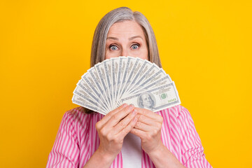 Photo of mature woman happy positive smile close cover face money cash currency isolated over yellow color background