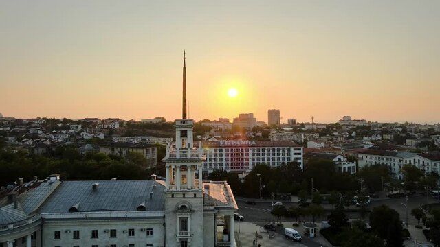 flight next to the golden spire of the clock tower of the Drama Theater at sunset. Old chapel in the city center. White chimes. Cinematic video from the air.