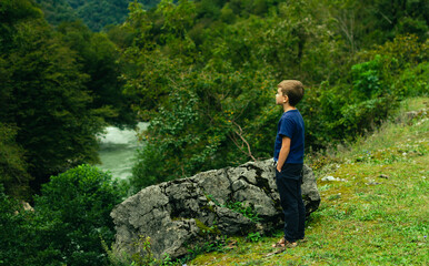 Naklejka na ściany i meble a boy stands at a large stone and looks at the mountains