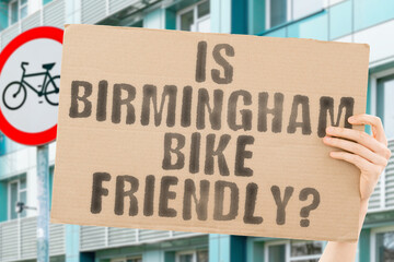 The question " Is Birmingham bike friendly? " on a banner in men's hand with blurred background. Transportation. Zero waste. Bicycle lane. Streets. City. Safety. Insecure. Road signs. Dangerous