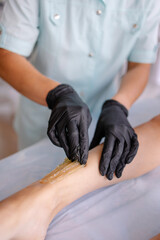 Naklejka premium Legs depilation with sugar paste. Close-up of lifestyle ankle hair removal process in the salon. Hands in black latex gloves. Shugaring procedure professional service. sugaring