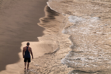 Fototapeta na wymiar Rear view of adult man walking on a beach with ocean wave during sunrise