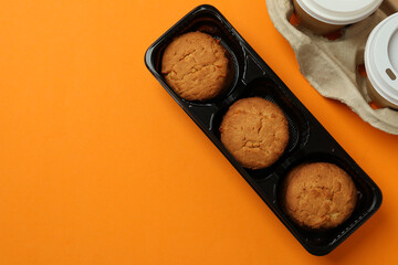 Cookies and paper cups of coffee on orange background