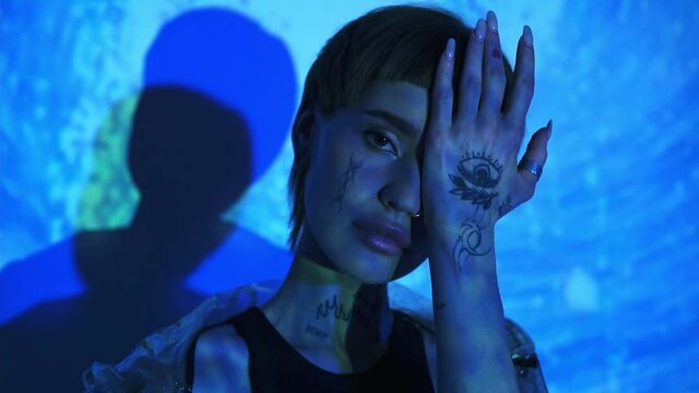 Tattooed model covering face with hand on abstract blue background 