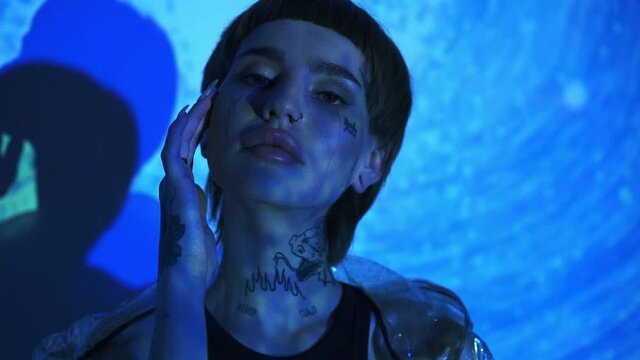 Young tattooed model touching face on abstract blue background 