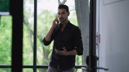 Dissatisfied bearded young business owner talking arguing on the phone gesturing standing in office indoors. Portrait of troubled Middle Eastern handsome man discussing project failures