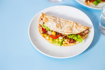 corn tortilla stuffed with meat and vegetables on a blue background. Taco