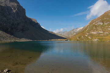 Mountain lake, moutains reflected in mirror-smooth water, steep rocks and alpine meadow