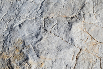 White big marble rock material with cracks close-up texture. Light stone surface pattern details in sunny Greece