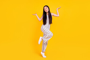 Fototapeta na wymiar Full length body size photo girl smiling in striped overall shrugging shoulders unsure isolated vibrant yellow color background