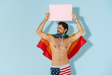 Young shirtless man with rainbow flag posing and showing placard