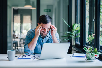 Businessman office working holding sore head pain from desk working and sitting all day using laptop computer or notebook suffering headache sick worker overworking concept