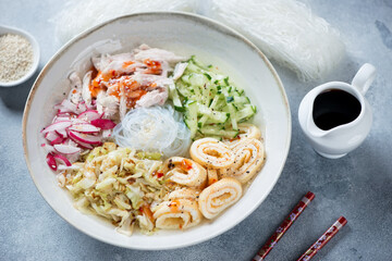 Plate of korean kuksi soup with chicken meat and chicken broth, studio shot on a light-blue stone background, selective focus