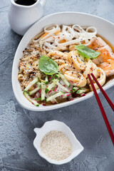 Bowl of cold korean traditional kuksi soup with chicken, vertical shot on a grey concrete background, close-up