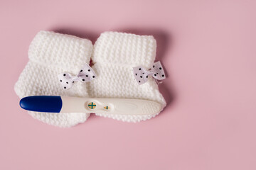 A positive pregnancy test and baby booties on a pink background. Waiting for the baby.