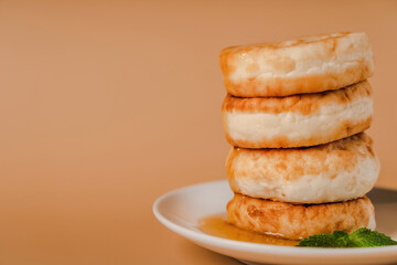 Cottage cheese pancakes on a plate with honey and mint on a beige background. Healthy and delicious morning breakfast. Traditional Russian food. Copyspace.