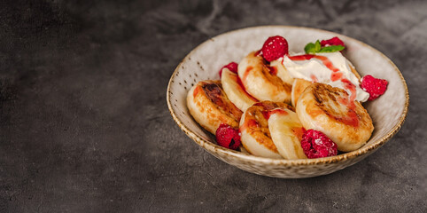 Delicious cottage cheese pancakes in a ceramic plate with yogurt and raspberries on a dark background 
