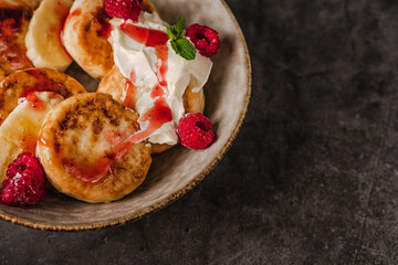 Delicious cottage cheese pancakes in a ceramic plate with yogurt and raspberries on a dark background 