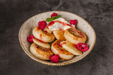 Delicious cottage cheese pancakes in a ceramic plate with yogurt and raspberries on a dark background 