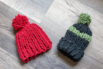 Two children's size knit hats on a wood surface.  Flat lay view of hand made winter accessories, red hat and green striped hat.