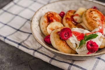 Delicious cottage cheese pancakes in a ceramic plate with yogurt and raspberries on a dark...