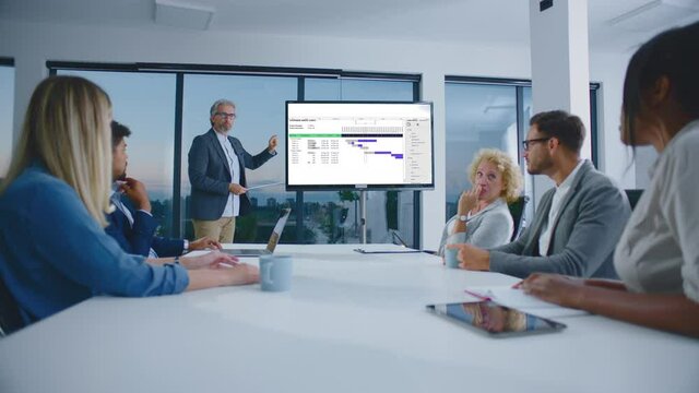 Colleagues sitting around table discussing during listening to presentation. Modern open space office interior.