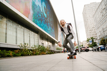 Grey mature man smiling while skateboarding at city street