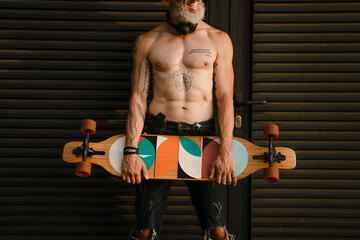 Shirtless mature man smiling while standing with skateboard