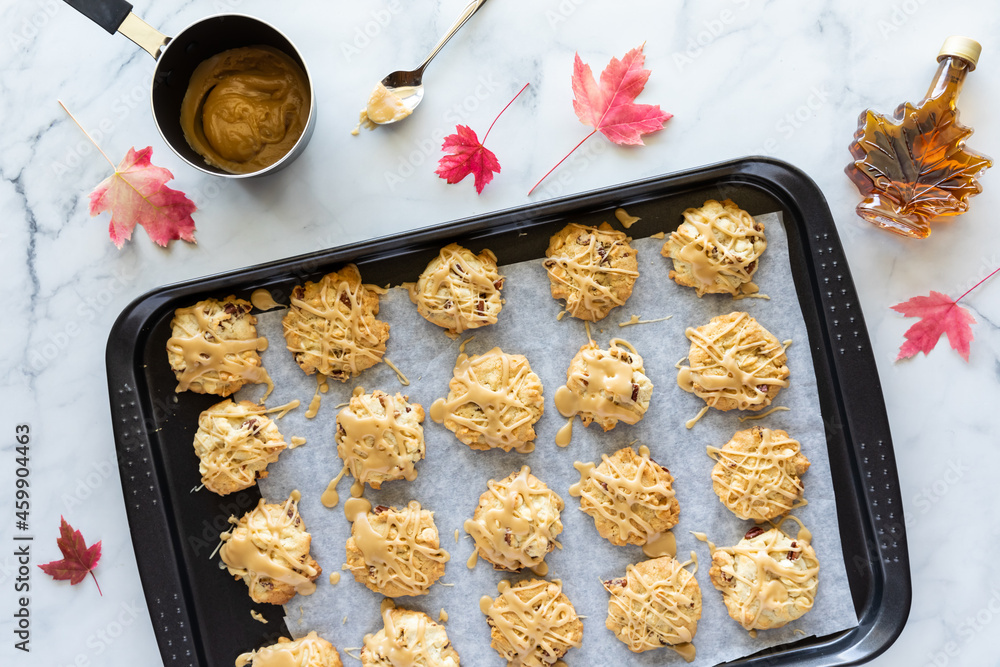 Poster top down view of a baking sheet of maple cookies drizzled with maple syrup, with maple leaves scatte