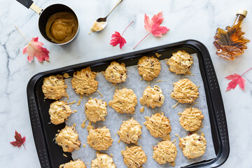 Top down view of a baking sheet of maple cookies drizzled with maple syrup, with maple leaves...