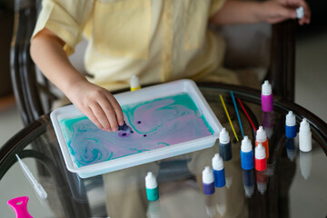 Drawing on water using the ebru technique. Creative development of children. Art therapy with kids. A boy in a yellow shirt draws with water paints